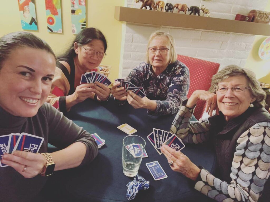 Four members of the Soroptimist International of Metropolitan Sacramento smiling at the camera while playing a card game at a table.