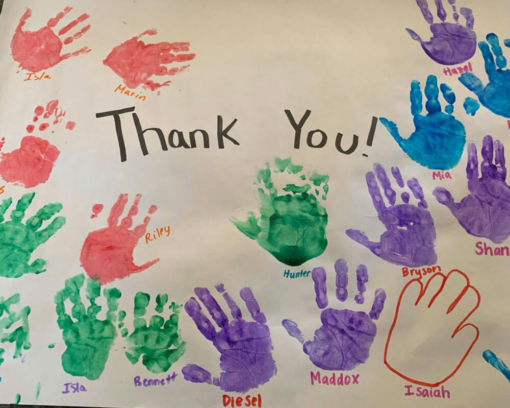 Close-up of a poster of children's hand prints with their names under them, around the words, "Thank You".