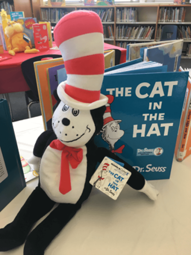 Close-up of a plush Cat in the Hat toy propped up on a table next to the book of the same name.